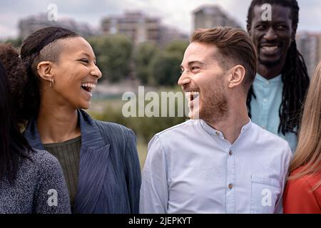 Gruppo di amici multietnici felici che sorridono e parlano spensierato - primo piano su una ragazza e un ragazzo che si guardano a ridere a voce alta - diversità e inclusivi Foto Stock