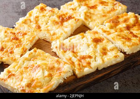 Torta di formaggio greco tradizionale con feta primo piano su un asse di legno sul tavolo. Orizzontale Foto Stock