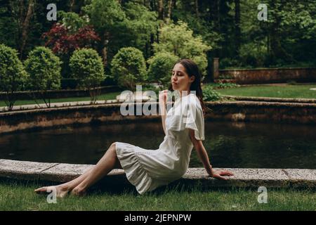 Bella giovane donna in abito seduto vicino stagno. Concetto di bellezza naturale Foto Stock