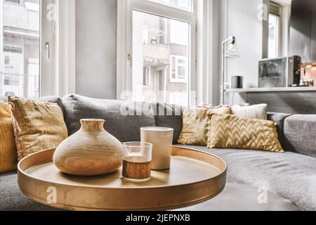 Ampio e morbido divano in velluto con cuscini colorati nel soggiorno con parquet in legno e cucina isolana sotto il soffitto con travi Foto Stock