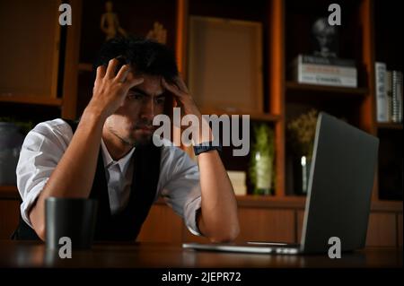 Stressato e serio uomo d'affari asiatico o direttore esecutivo maschile pensiero pensivo sul suo piano d'investimento di affari alla sua scrivania d'ufficio. Foto Stock