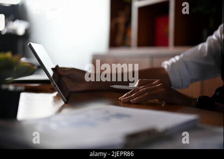 Immagine ritagliata, un uomo d'affari asiatico o un imprenditore maschile seduto alla sua scrivania, utilizzando un tablet digitale portatile. Foto Stock