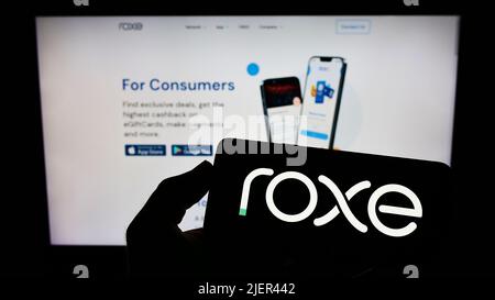 Persona che tiene lo smartphone con il logo della società americana Roxe Holding Inc. Sullo schermo di fronte alla pagina Web. Mettere a fuoco sul display del telefono. Foto Stock