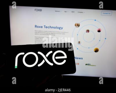 Persona che detiene il cellulare con il logo della società di pagamento statunitense Roxe Holding Inc. Sullo schermo di fronte al sito web aziendale. Mettere a fuoco sul display del telefono. Foto Stock