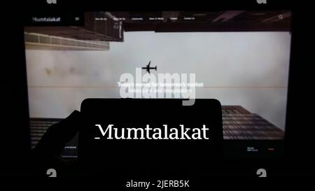 Persona che tiene lo smartphone con il logo della Bahrain Mumtalakat Holding Company sullo schermo di fronte al sito web. Mettere a fuoco sul display del telefono. Foto Stock