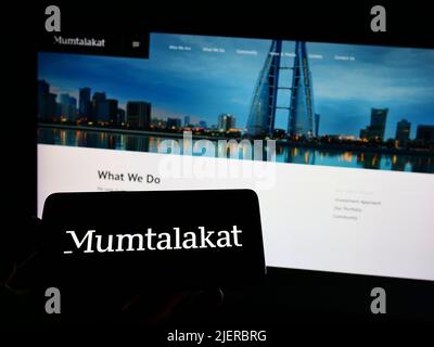 Persona che tiene il cellulare con il logo di Bahrain Mumtalakat Holding Company sullo schermo di fronte al sito web aziendale. Mettere a fuoco sul display del telefono. Foto Stock