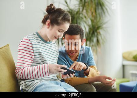 Ritratto di due bambini, ragazzo e ragazza con smartphone a scuola durante la pausa, entrambi vestiti con abiti colorati Foto Stock