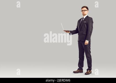 Ritratto di serio manager professionale maschile con laptop in mani su sfondo grigio. Foto Stock