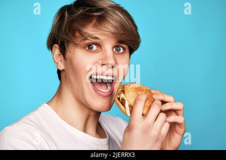 Giovane molto affamato che tiene gustoso hamburger Foto Stock