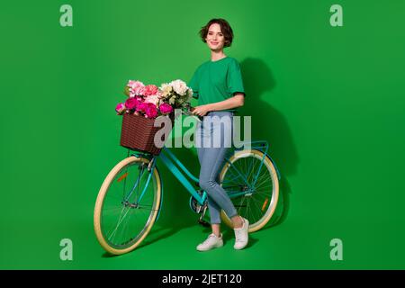 Foto a grandezza naturale di bella ragazza in piedi vicino alla bicicletta hanno buon umore isolato su sfondo verde Foto Stock