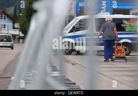 Garmisch Partenkirchen, Germania. 28th giugno 2022. Una donna anziana cammina con una borsa vicino alle barriere e di fronte ad una macchina della polizia. La Germania ha ospitato il vertice del G7 a Schloss Elmau. Credit: Karl-Josef Hildenbrand/dpa/Alamy Live News Foto Stock