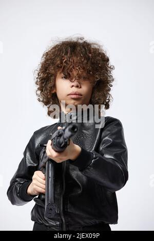 Giovane uomo afro-americano bello indossando abiti casual che tengono la pistola, giocando uccidendo armi da tiro Foto Stock