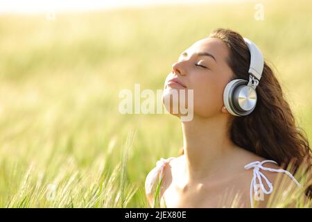 Donna rilassata con cuffie wireless che meditano in un campo di grano Foto Stock