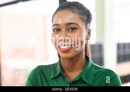 Primo piano ritratto di fidata dipendente afroamericano in piedi in moderno spazio ufficio, allegro attraente donna d'affari nera in camicia verde guarda la fotocamera con un sorriso leggero amichevole Foto Stock