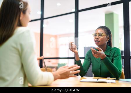 Giovane entusiasta dirigente afro-americano in occhiali spiega la nuova strategia per i dipendenti e gesturing. Ritratto interno di diversi team di lavoro brainstorming nella moderna sala riunioni Foto Stock