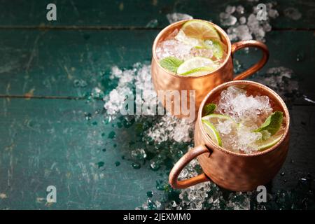 Da sopra di bevande alcoliche mulo Mosca con fette di lime e ghiaccio servito in tazze di rame su tavolo di legno shabby Foto Stock