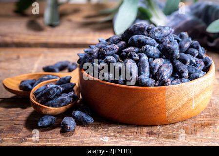 Ciotola con fresco fattoria Haskap bacche, giardino coltivato miele, miele, su sfondo legno copia spazio Foto Stock