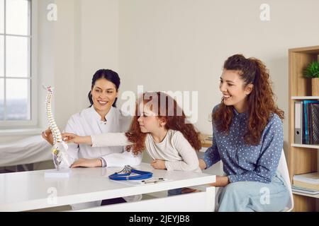 Donna felice e il suo bambino piccolo che guarda il modello umano della spina dorsale all'ufficio del medico Foto Stock