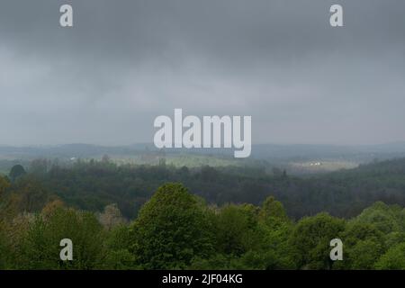 Zone luminose di sole su una campagna collinare, colline ricoperte di lussureggianti foreste, nebbia mattutina e nuvole cupe Foto Stock