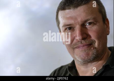 Un ritratto di un uomo tranquillo e sorridente contro un muro grigio chiaro. Un maschio di mezza età con capelli corti e grigi. L'uomo felice guarda nella fotocamera. P Foto Stock