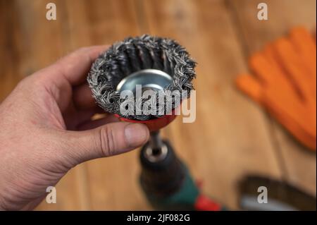 L'uomo ha messo in su la spazzola di filo della tazza del nodo nella camma di un mandrino di trapano elettrico. Utensile per la lavorazione del legno, la levigatura, la rimozione della ruggine dalle varie superfici. Primo piano. Selezionare Foto Stock