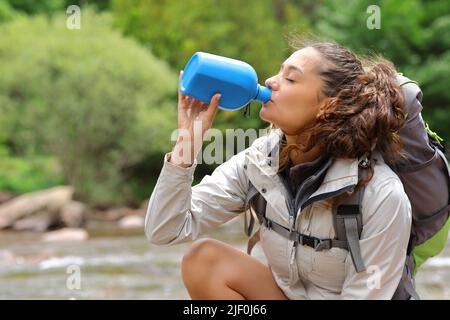 Vista laterale ritratto di un tekker bere acqua dalla bottiglia in un fiume Foto Stock