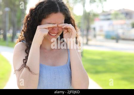 Donna stressata graffiando occhi itchy mentre cammina in un parco Foto Stock