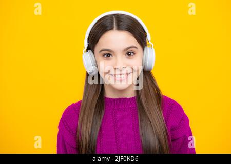 Adolescente in moderne cuffie wireless che ascolta la musica delle canzoni nell'app audio, ascoltando la sua musica preferita su sfondo giallo dello studio. Foto Stock