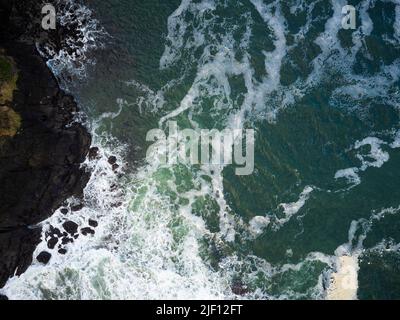 Riprese da un drone. Una splendida superficie dell'oceano turchese con onde bianche e schiumose che si infrangono su una costa rocciosa irregolare. Bellezza della natura, mare. Foto Stock