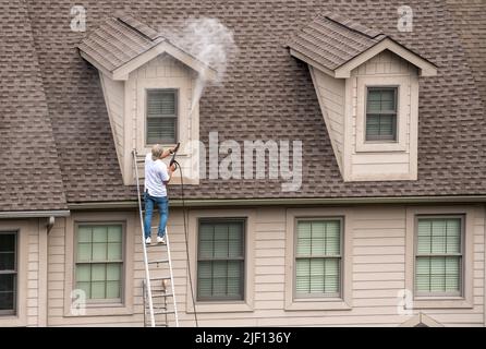 Verniciatore su scala usando lo spray di lavaggio a pressione per pulire il legno prima di verniciare la casa Foto Stock