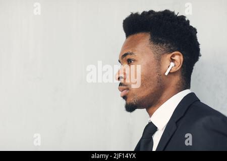 Vista laterale del giovane uomo d'affari nero serio e intenzionale nelle cuffie senza fili che contemplano intorno Foto Stock