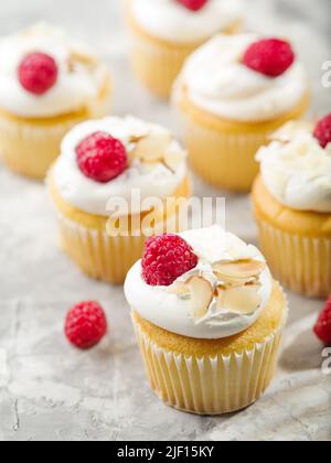 Un sacco di muffin con panna montata, lamponi rossi freschi e pezzi di mandorle su sfondo bianco. Un sacco di oggetti. Cibo festivo, banchetti, picnic. ADV Foto Stock