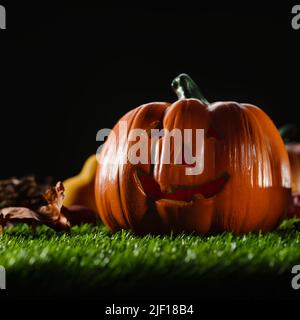 Su un prato verde, un arancio sorridente zucca di Halloween, coni e foglie d'autunno contro un cielo notturno nero e cupo. Celebrazione delle vacanze autunnali - ha Foto Stock