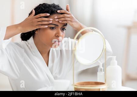 Problema Skin. La donna frustrato ha notato il pimple sulla fronte mentre osserva nello specchio Foto Stock