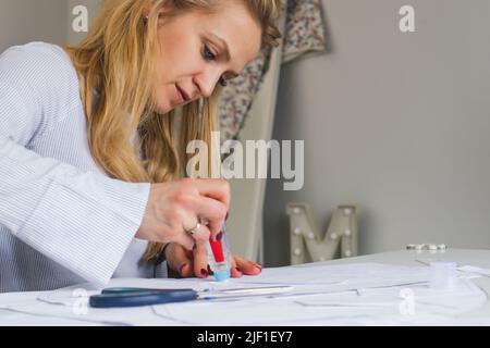 Donna su misura durante il lavoro su modelli di cucitura. Unire i dettagli della carta per vestire Foto Stock