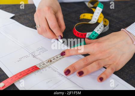 Il dressmaker contrassegna un pezzo di tessuto con gesso in base al modello di carta. Lavoro di sarto, utensili per cucire Foto Stock