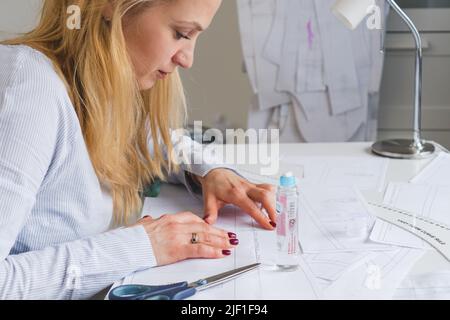 Donna su misura durante il lavoro su modelli di cucitura. Unire i dettagli della carta per vestire Foto Stock