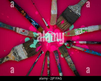 Composizione orizzontale in cui alcuni pennelli vecchi e usati di varie dimensioni appaiono su sfondo magenta o fucsia e con vernice rosa e verde chiaro Foto Stock