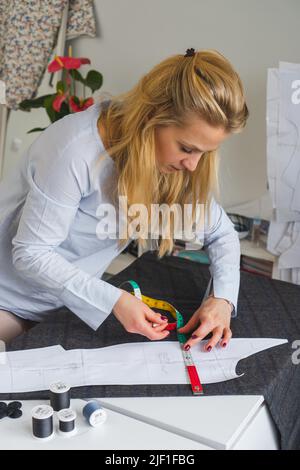 Il dressmaker contrassegna un pezzo di tessuto con gesso in base al modello di carta. Lavoro di sarto, utensili per cucire Foto Stock