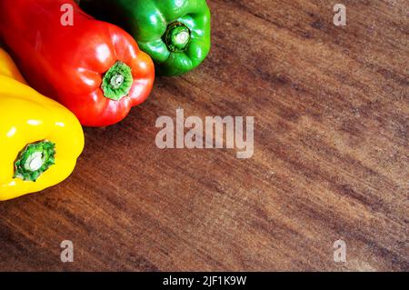 Tre peperoni di colori diversi nell'angolo superiore sinistro della foto in cima ad un tavolo marrone Foto Stock