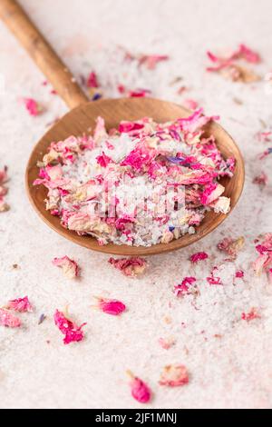 Vedi il wih di sale con petali di fiori secchi in paletta di legno sul tavolo di marmo rosa Foto Stock