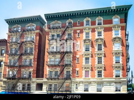 Edificio residenziale in mattoni rossi all'angolo tra 5th Ave e W 120 st, Harlem, Manhattan, NYC, con scale di emergenza in metallo nero. Foto Stock