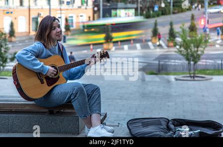 Musicista femminile che suona la chitarra acustica e canta all'aperto in strada. Foto Stock