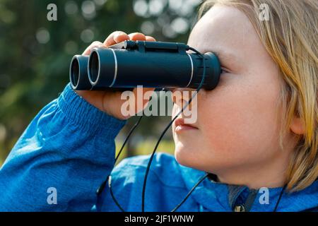 Bambini che guardano attraverso binocoli nel parco. Primo piano ritratto di un ragazzo che esplora la fauna selvatica. Bird watching, escursioni, e concetto di avventura. Foto Stock