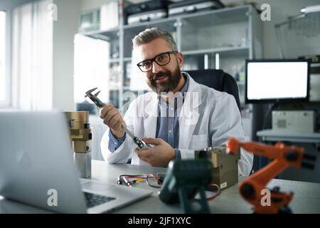 Un ingegnere di robotica che lavora alla desing del braccio robotico moderno adn seduto al dest in laboratorio. Foto Stock