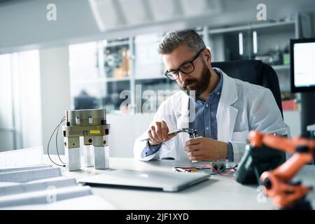 Ingegnere robotico che lavora alla desing di un moderno braccio robotico seduto alla scrivania in laboratorio. Foto Stock