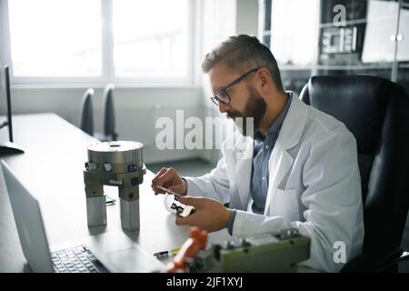 Ingegnere robotico che lavora alla desing di un moderno braccio robotico seduto alla scrivania in laboratorio. Foto Stock