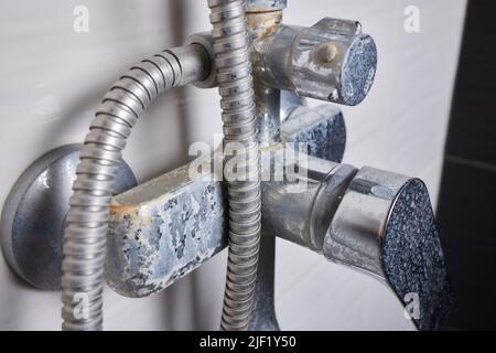 Un flusso sottile di acqua dura fluisce da un vecchio aeratore del rubinetto. Vecchio bagno rubinetto di sink contaminato con calcio e sporcizia Foto Stock