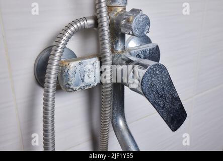 Un flusso sottile di acqua dura fluisce da un vecchio aeratore del rubinetto. Vecchio bagno rubinetto di sink contaminato con calcio e sporcizia Foto Stock