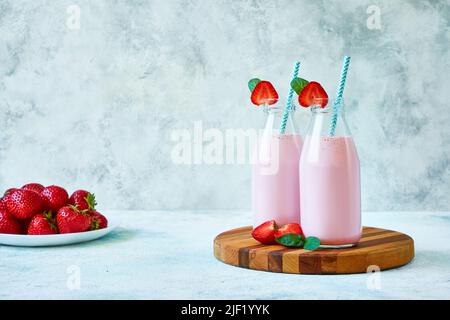 Frullato alla fragola o milkshake in vaso di vetro con frutti di bosco su fondo di cemento blu Foto Stock